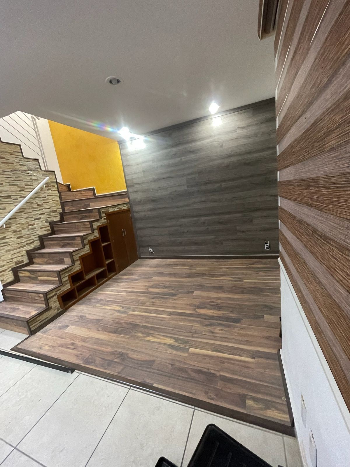 Interior space with wooden flooring and staircase, featuring wall panels and ceiling lights.